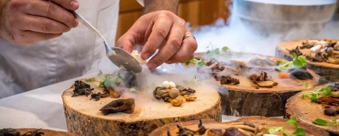 A chef is plating a dish on wood slices with dry ice smoke