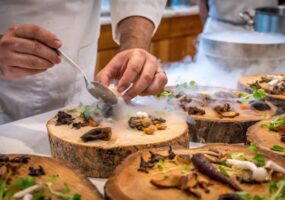 A chef is plating a dish on wood slices with dry ice smoke