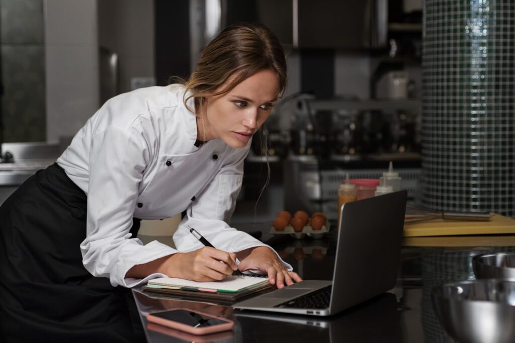 Female chef in the kitchen using laptop