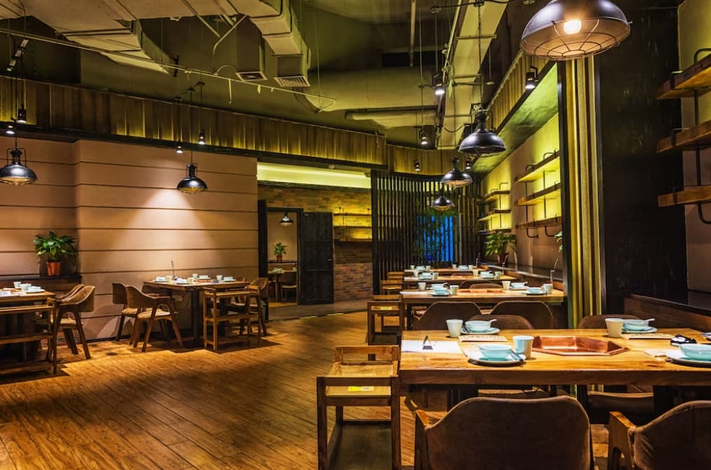 A cozy, dimly lit restaurant with wooden tables and pendant lighting