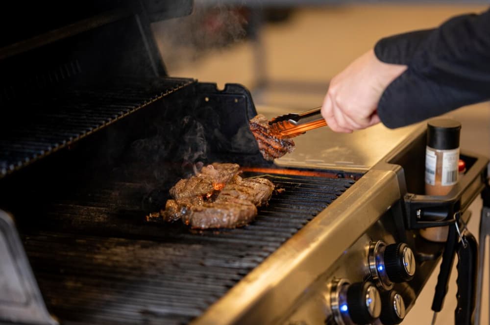 persons hands in black clothing  holding a meat over the grill