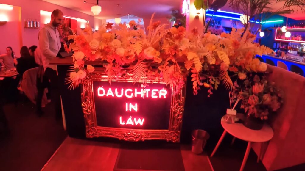 A vibrant bar with a neon sign "Daughter in Law" surrounded by lavish floral decorations