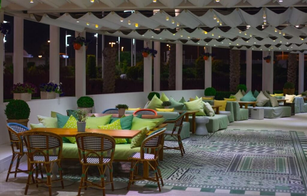 An inviting outdoor lounge area with green pillows and patterned rugs under soft lighting