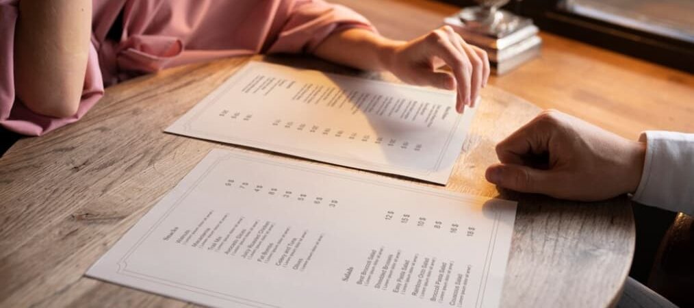 Two people looking at menus on a wooden table in a cozy setting