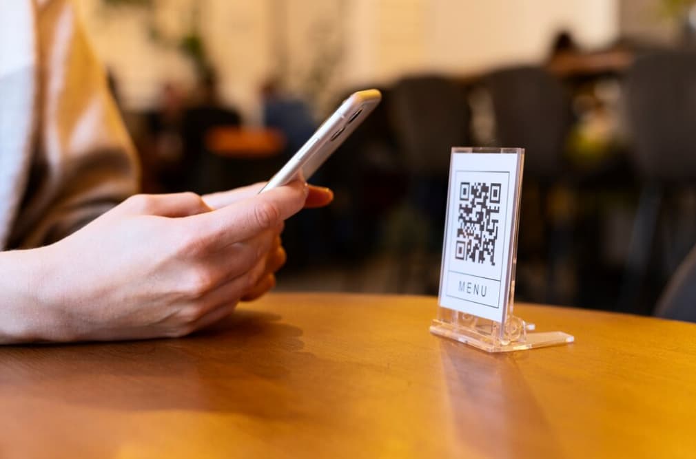 A person scanning a QR code menu on a clear stand at a cafe