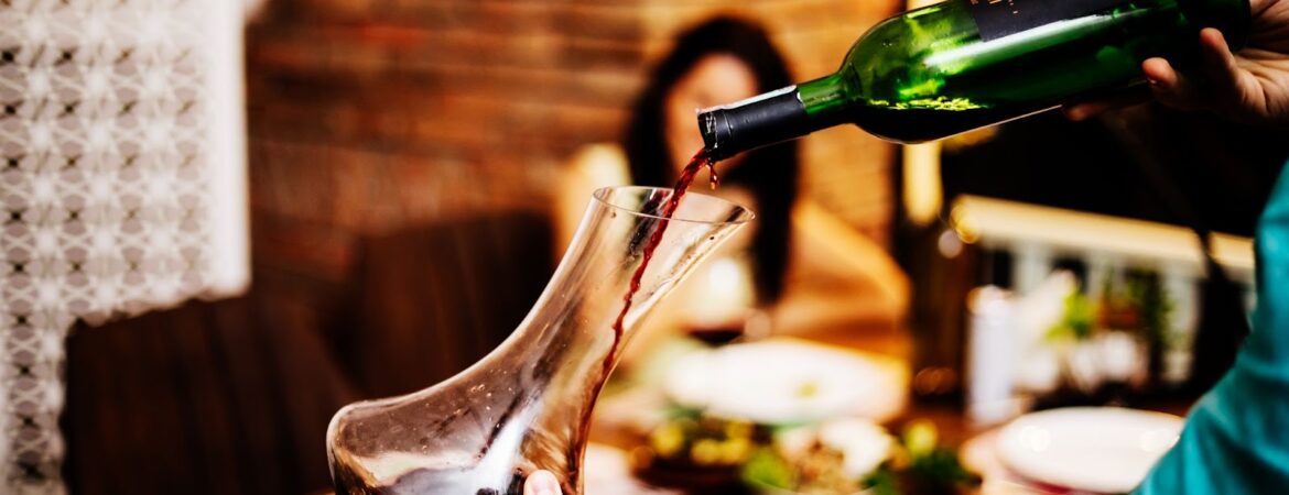 Man putting red wine from bottle into glass jar