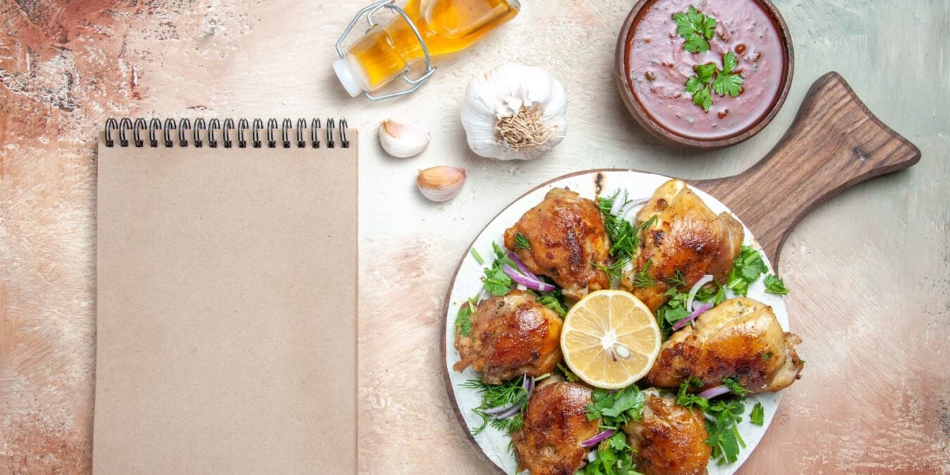 Top view of chicken with herbs and oil, garlic sauce and notebook