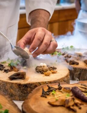 A chef is plating a dish on wood slices with dry ice smoke
