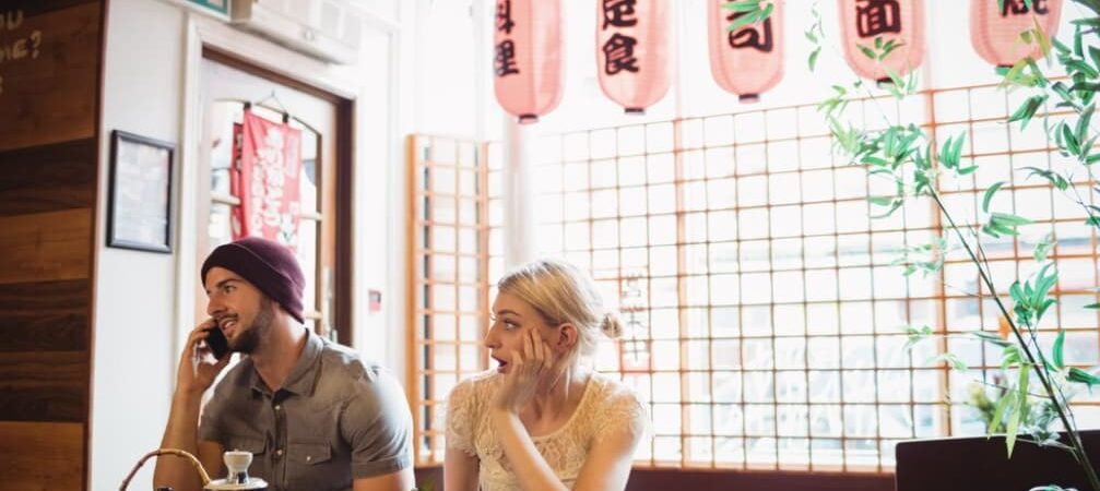 Two people at a restaurant table with sushi, one on a phone call