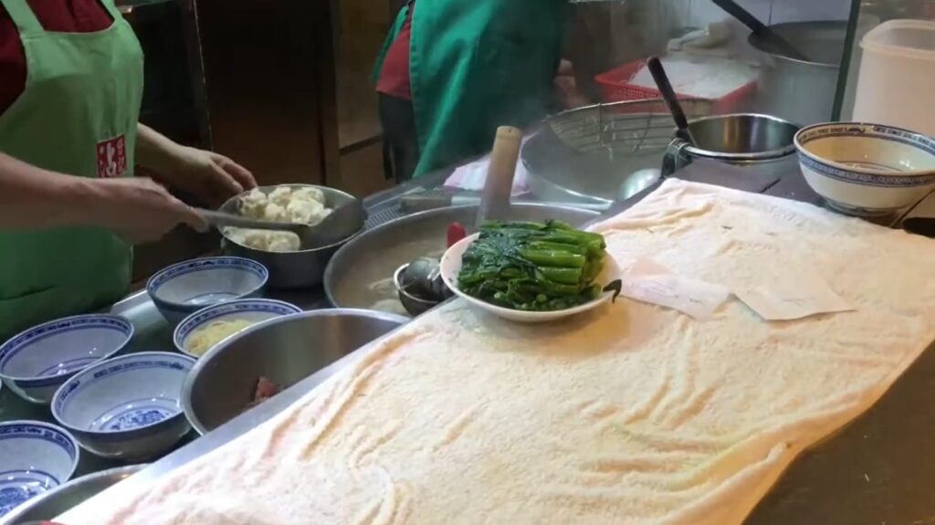 A bustling kitchen scene with chefs preparing dumplings and vegetables