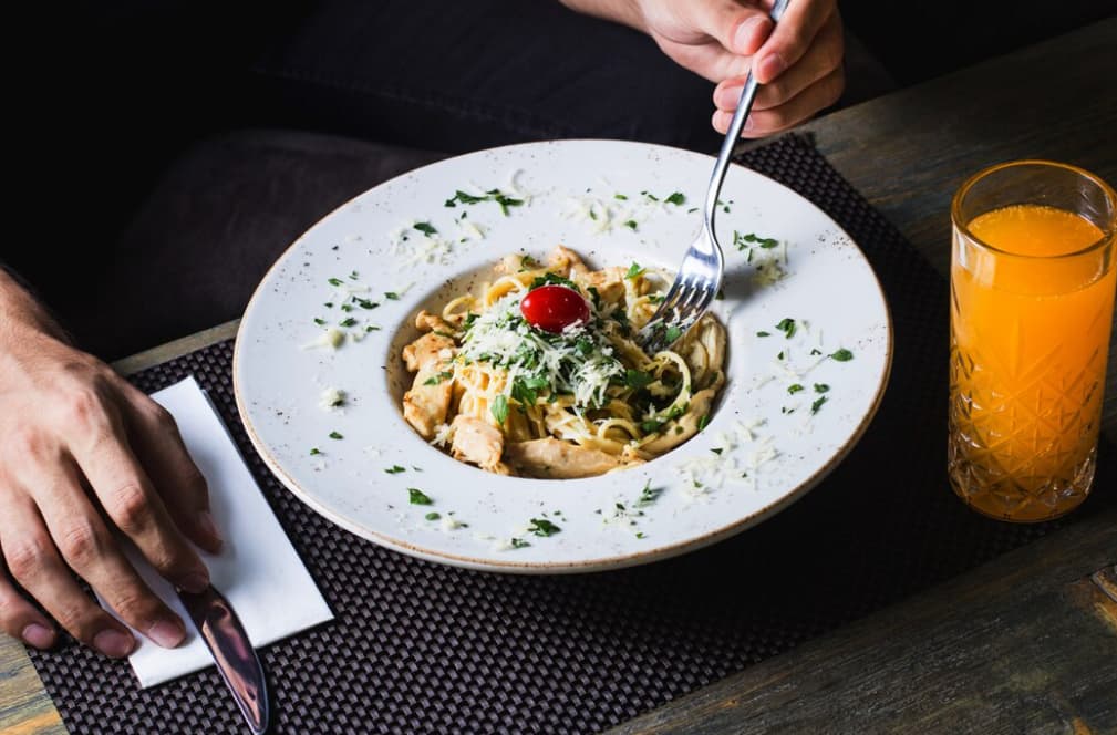A person at a dark table about to eat pasta with a glass of orange juice
