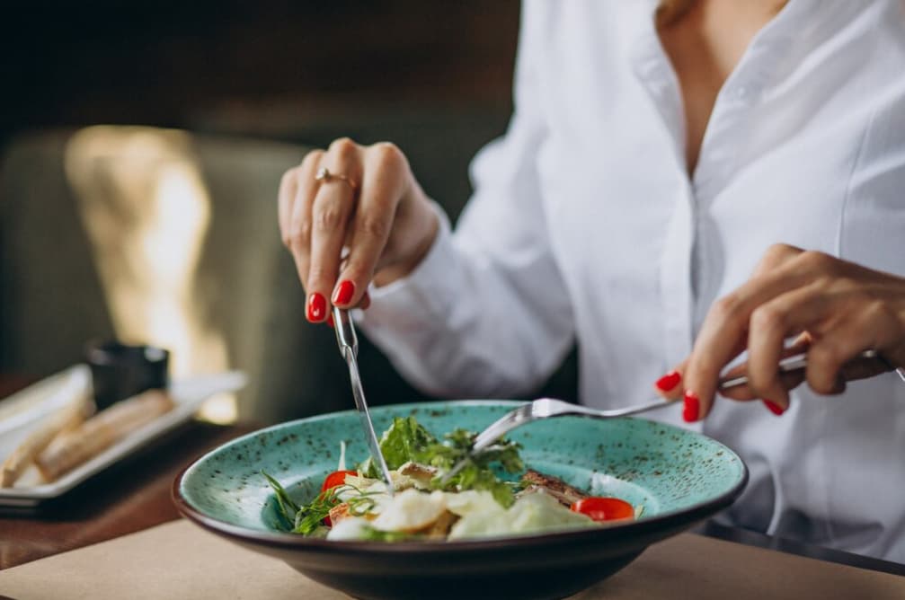A person dining, focusing on a salad with a fork