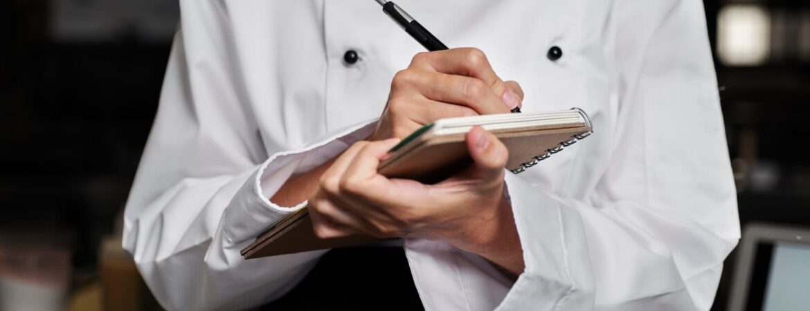 Chef in the kitchen taking notes with pen and notebook