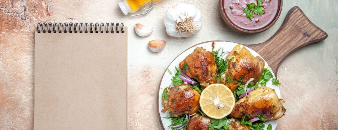 Top view of chicken with herbs and oil, garlic sauce and notebook