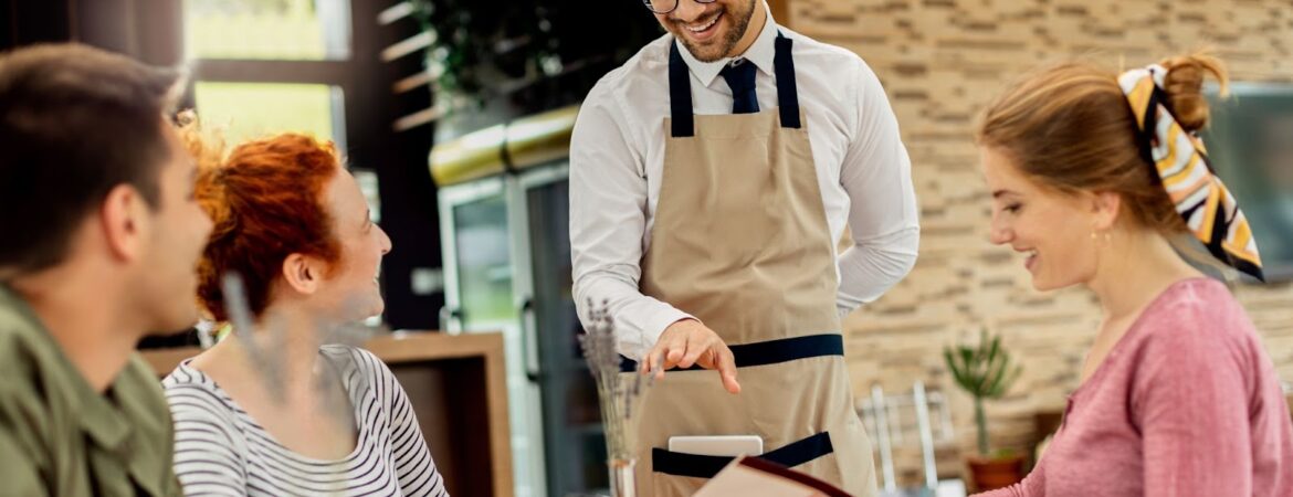 Happy waiter communicating with group of customers in a cafe