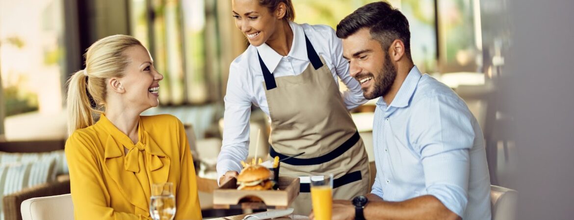 Young happy waitress serving food to guests in a restaurant