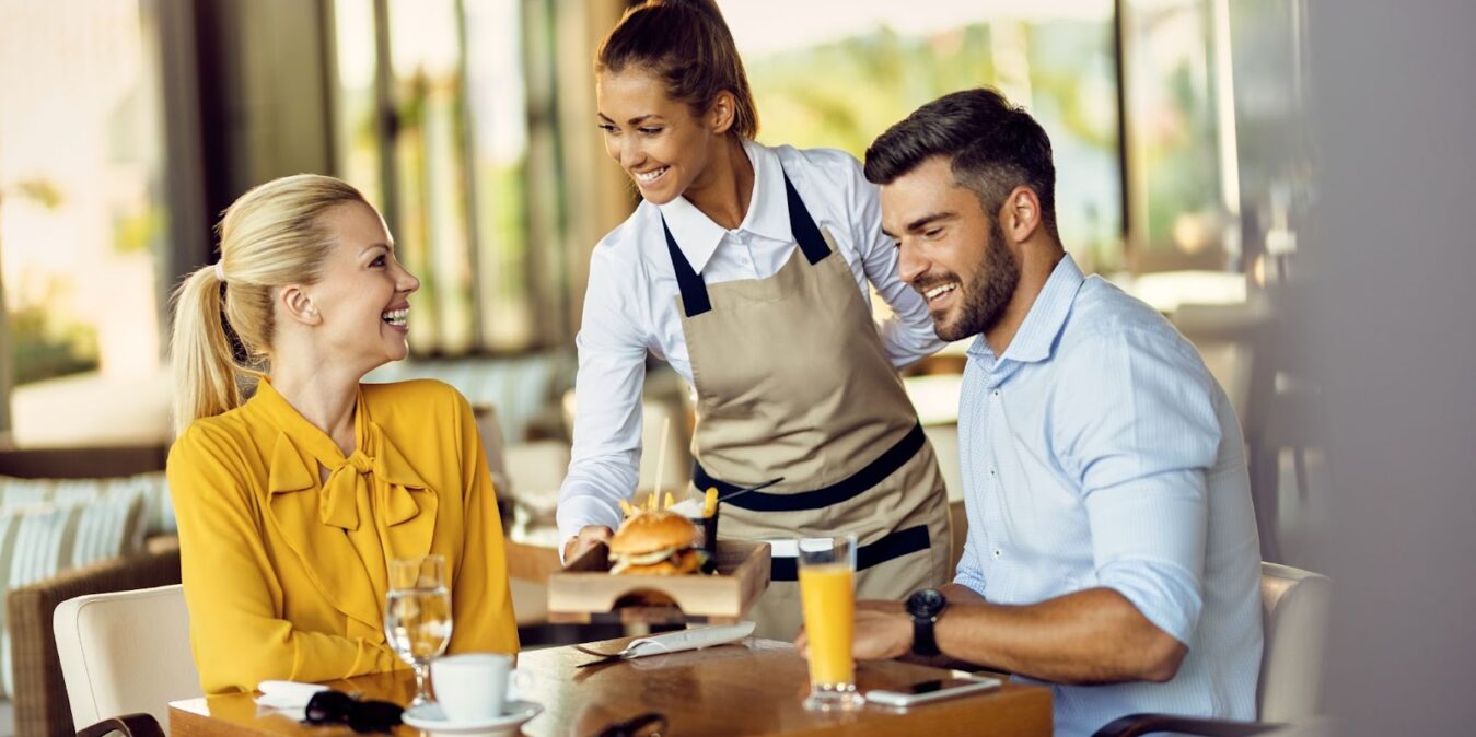 Young happy waitress serving food to guests in a restaurant